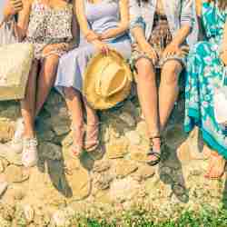 Four Women In Dresses Sitting On A Rock Wall