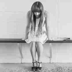 Black and white photo of a girl sitting on a bench with her head hung down