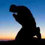 Shadow of Man Kneeling In Prayer During A Sunset