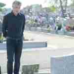 Man In Graveyard Looking At A Tombstone