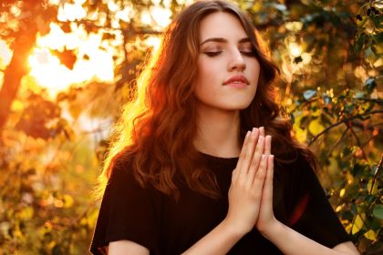 Young Woman praying In Nature with her eyes closed